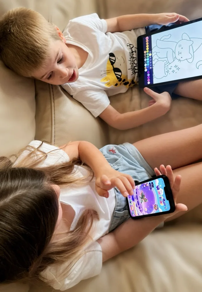The founder's two young nephews side by side on a couch, one colouring a puppy in WimziPal on an iPad, the other playing WimziPal on a phone